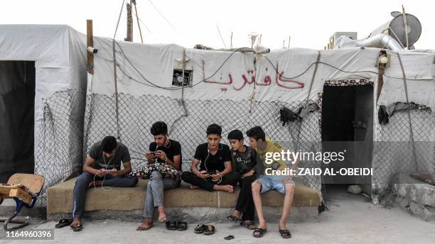 Boys play on cell phones as they sit outside a cafeteria tent at a camp for internally displaced persons of Iraq's Yazidi minority in the Sharya...