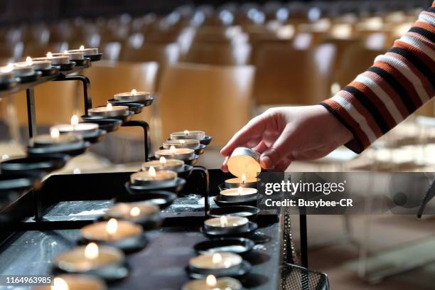 a young person lighting a candle in a cathedral - candle vigil stock pictures, royalty-free photos & images