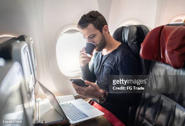 man working in airplane using cellphone and drinking coffee - mobile on plane stock pictures, royalty-free photos & images