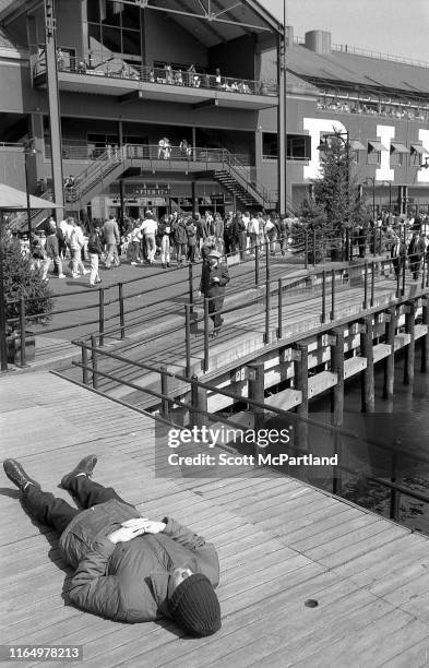 View of an unidentified man, his knit cap pulled down over his eyes, as he lies in a pedestrian walkway for a nap at Pier 17, South Street Seaport,...