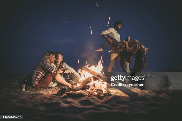 coppie felici che si divertono in una festa notturna in spiaggia vicino al falò. - bon fire foto e immagini stock