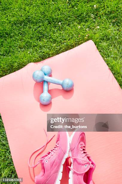 high angle view of dumbbells and sport shoes on red exercise mat on a meadow - tapis de sol photos et images de collection