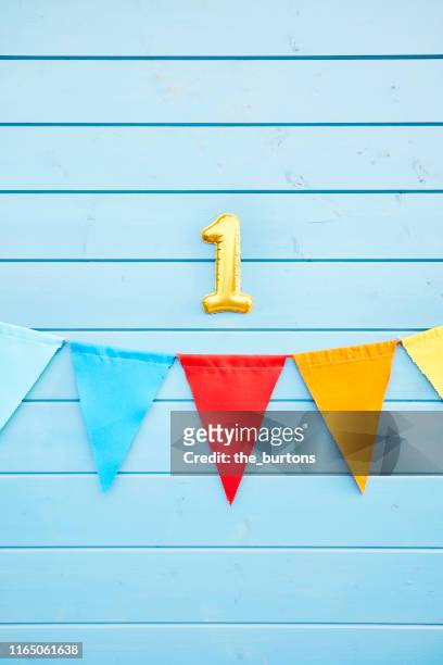 colorful bunting flags/ pennant chain for party decoration and gold colored number one at blue painted wooden wall - about you awards in hamburg stock pictures, royalty-free photos & images