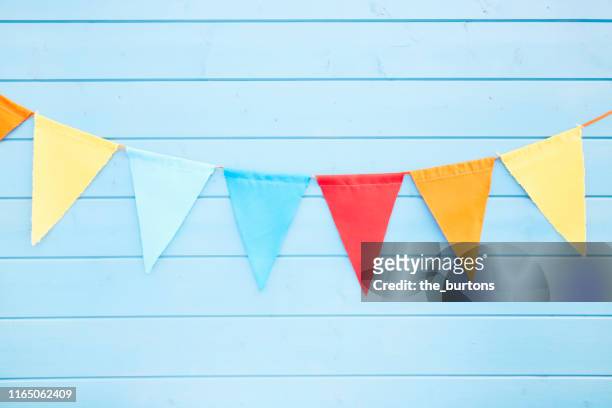 colorful bunting flags/ pennant chain for party decoration at blue painted wooden wall - party decorations stock-fotos und bilder