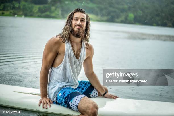 knappe surfer met surfplank in de zee - sitting on surfboard stockfoto's en -beelden