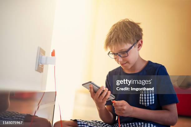 little boy plugging smartphone to a charger at home - electrical outlet stock pictures, royalty-free photos & images