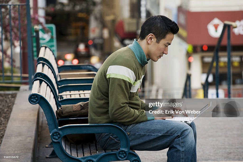 Young asian man on a park bench with laptop