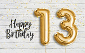 Happy 13th birthday gold foil balloon greeting white wall background.