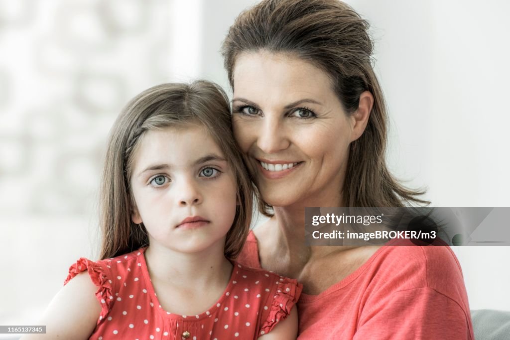 Mother and daughter sit together on the couch and look into the camera, smile, Germany
