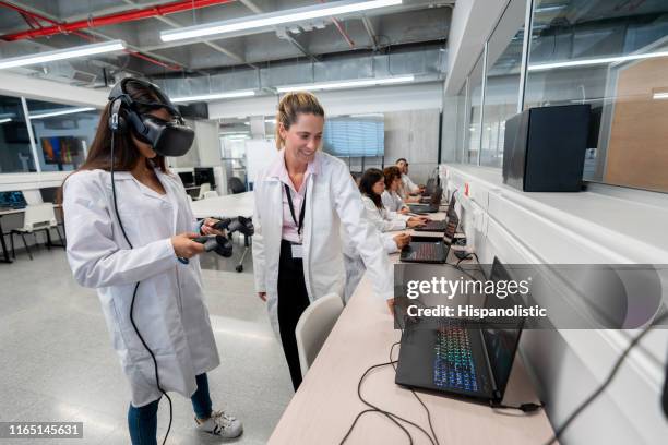 adult female teacher using laptop while student experiments with virtual reality simlator and joysticks - virtual reality classroom stock pictures, royalty-free photos & images