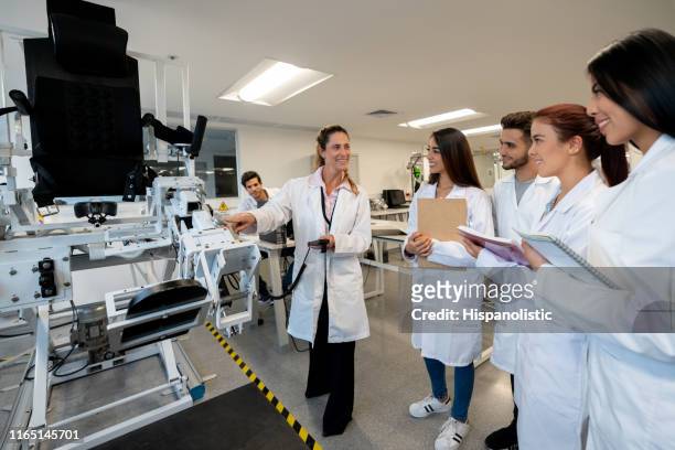 profesora alegre explicando cómo funciona una máquina en el laboratorio de biomecánica mientras los estudiantes prestan atención - mechatronics fotografías e imágenes de stock