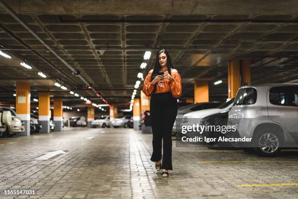 mujer joven caminando y usando el teléfono inteligente en el estacionamiento - lot of people fotografías e imágenes de stock