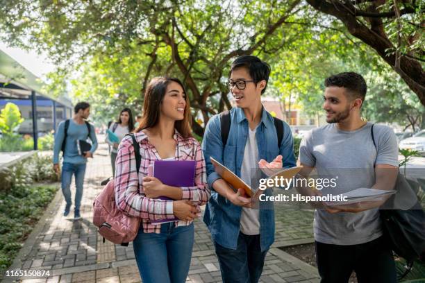 young students at the college campus walking to class holding their books open discussing something - college students diverse stock pictures, royalty-free photos & images