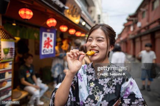 mujer joven en yukata comiendo dango japonés dumpling en la calle - comida japonesa fotografías e imágenes de stock