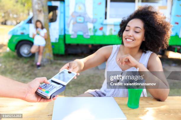 smiling afro woman paying with smart phone - food truck payments stock pictures, royalty-free photos & images