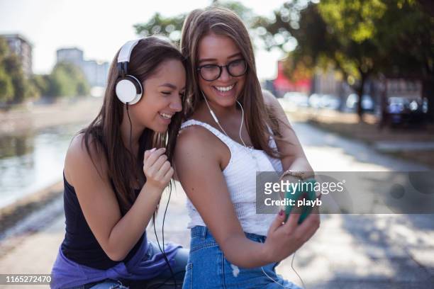 best friends together outdoors listening to music - sharing headphones stock pictures, royalty-free photos & images