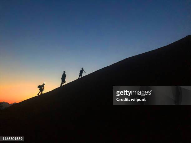 jungen silhouette skalieren einen steilen hügel bei sonnenuntergang - pinnacle stock-fotos und bilder