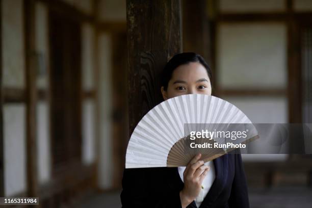 young woman covering face with korean traditional fan - south asian man stock-fotos und bilder