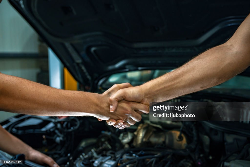 Car mechanic handshakes customer