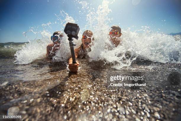 kids playing in sea waves and filming themselves using waterproof action camera. - family selfie stock pictures, royalty-free photos & images