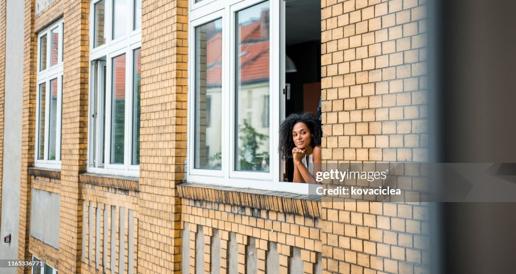 Glückliche afrikanische Geschäftsfrau steht am Fenster und bewundert die Aussicht