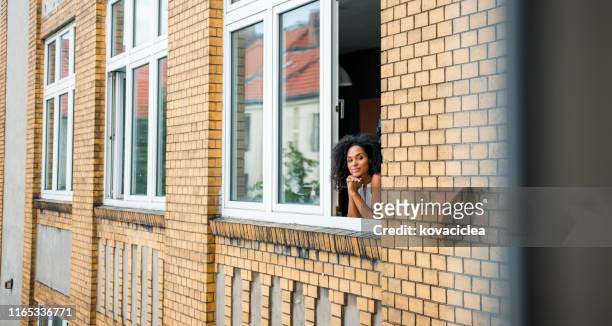 glückliche afrikanische geschäftsfrau steht am fenster und bewundert die aussicht - fenster offen stock-fotos und bilder