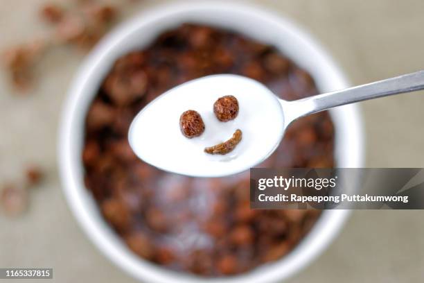 smiling chocolate cereals in the spoon with cereals in a bowl on background - bowl of cornflakes stock-fotos und bilder