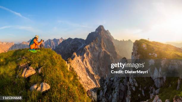 bergfotograf bei sonnenuntergang mit blick auf watzmann und gipfelkreuz des großen hundstods - bavarian alps stock-fotos und bilder