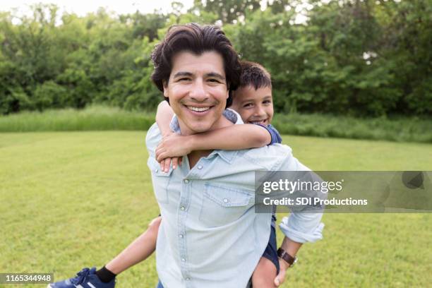 while uncle carries nephew, both smile for camera - uncle nephew stock pictures, royalty-free photos & images