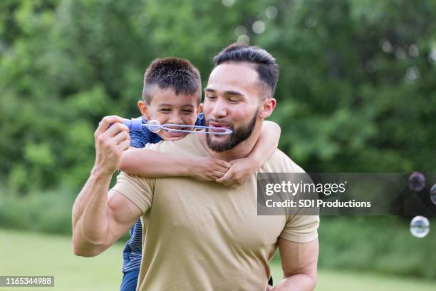 mid adult father and young son blow bubbles at park - uncle nephew stock pictures, royalty-free photos & images