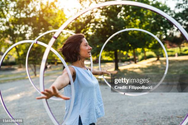 young adult woman juggling with hula hoop at the public park - woman juggling stock pictures, royalty-free photos & images