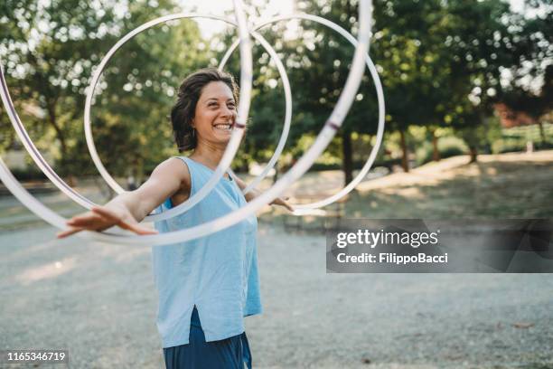 jong volwassen vrouw jongleren met hula hoop in het openbare park - juggling stockfoto's en -beelden