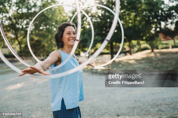 young adult woman juggling with hula hoop at the public park - malabarismo imagens e fotografias de stock