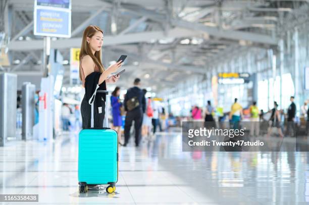 young businesswoman using mobile phone with suitcase in airport terminal - 1990 lounge stockfoto's en -beelden