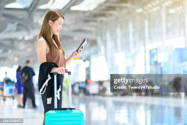 young businesswoman using mobile phone with suitcase in airport terminal - 1990 lounge stockfoto's en -beelden