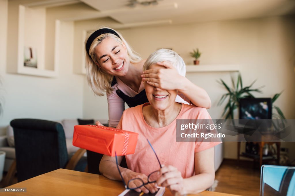 Niña cubriendo los ojos de la madre y dándole el regalo