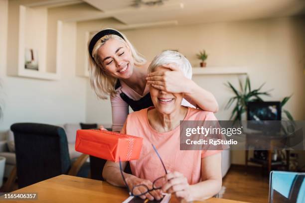 girl covering mother's eyes and giving her present - woman hold box imagens e fotografias de stock