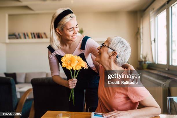 junge frau gibt ihrer mutter blumen - mothers day stock-fotos und bilder