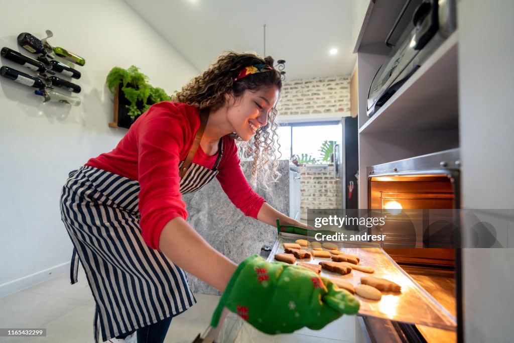 Happy woman putting Christmas cookies in the oven