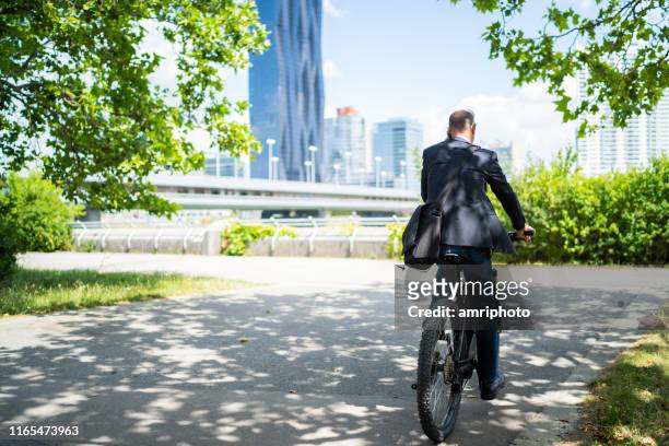 duurzame levensstijl, back view business man op weg naar werken aan elektrische fiets in stedelijk park - carbon neutrality stockfoto's en -beelden