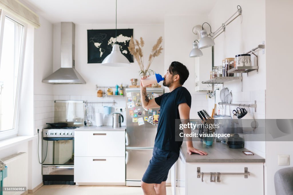 Asian man drinks protein shake after home workout