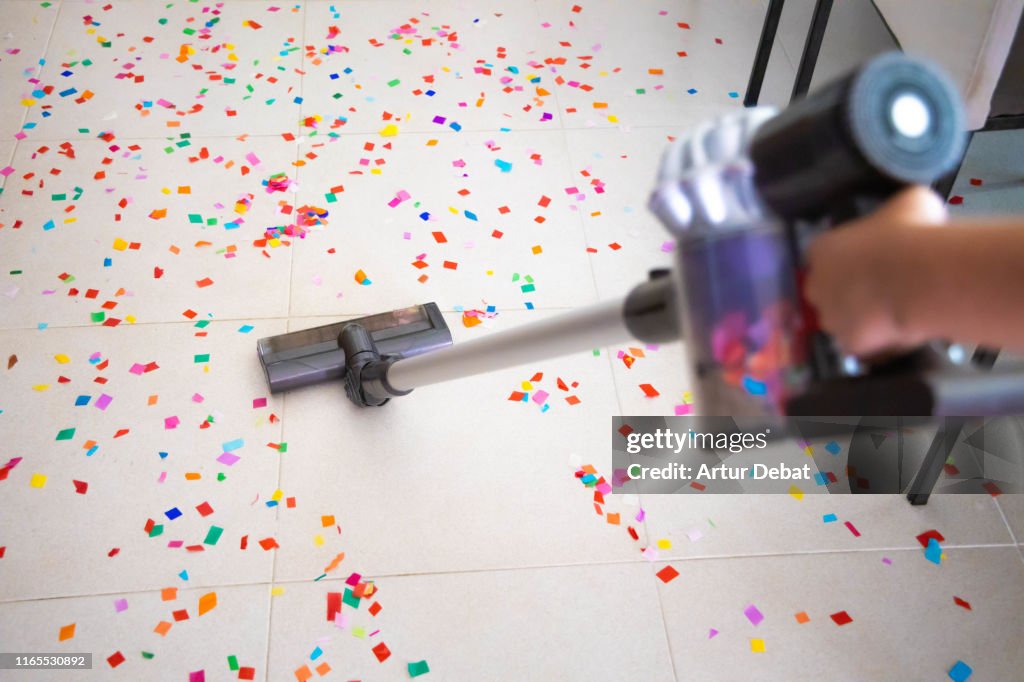 Cleaning home floor with vacuum after party with confetti.