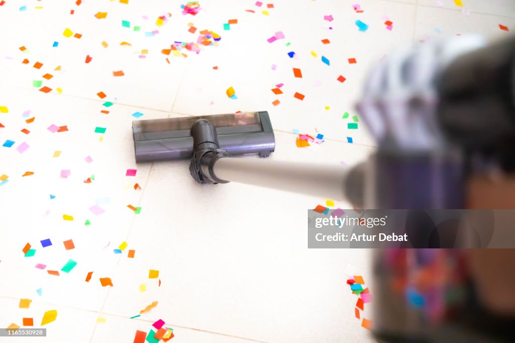 Cleaning home floor with vacuum after party with confetti.