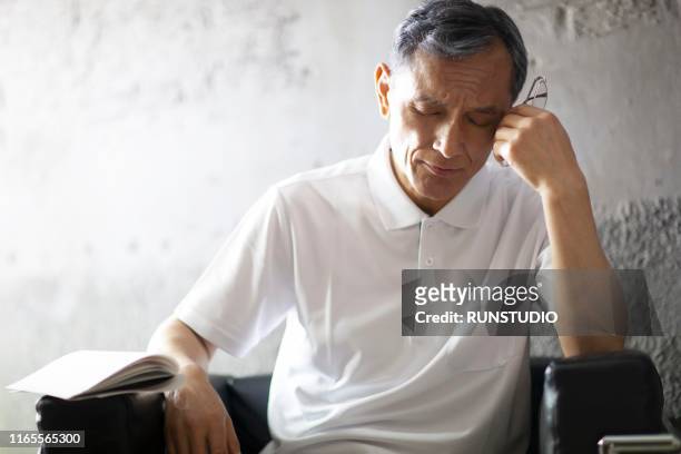 tired,stressed middle aged man sitting on chair - matt japan stock-fotos und bilder