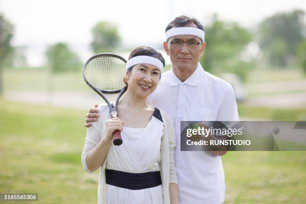 portrait of mature couple standing with tennis racket and ball - japanese tennis stock-fotos und bilder