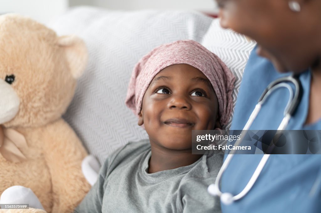 Smiling boy with cancer comforted by female doctor of African descent