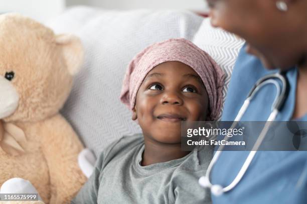 smiling boy with cancer comforted by female doctor of african descent - childhood cancer stock pictures, royalty-free photos & images