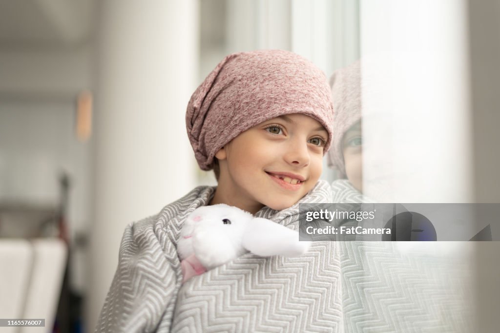 Lächelndes Mädchen mit Krebs schaut aus dem Fenster