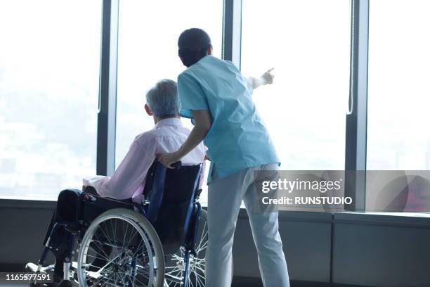 nurse and senior man in wheelchair looking through window - elderly care japanese photos et images de collection