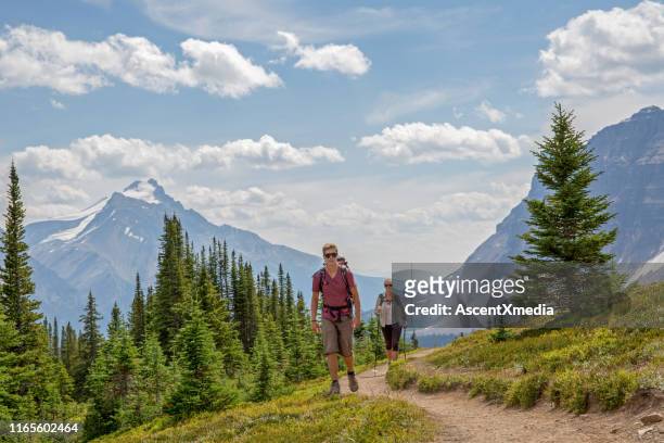 hikers ascend trail through an alpine meadow above the mountains - banff national park stock pictures, royalty-free photos & images
